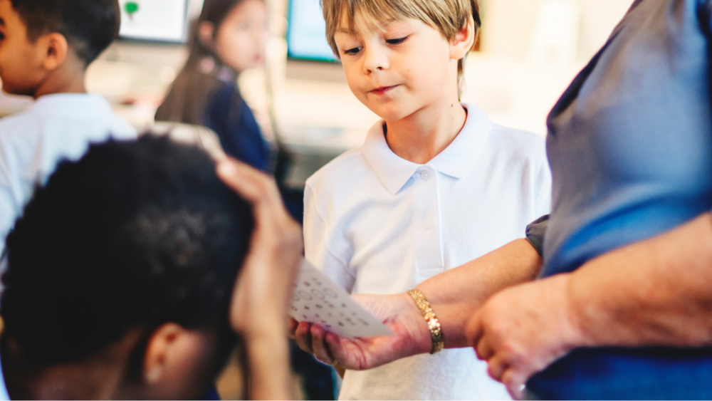 Primary school student reading a piece of paper shown to him by a member of staff