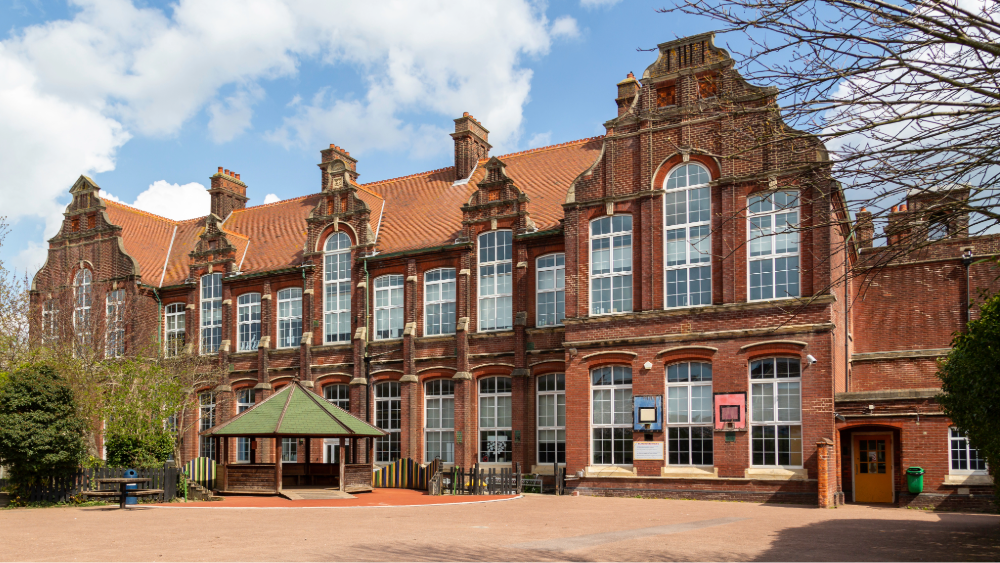 Outside of an old brick school building with two floors and a gazebo outside