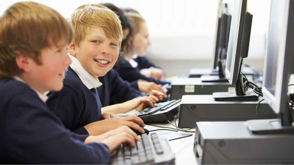 Young secondary students in an ICT class working on computers, one child is looking at the camera and smiling.