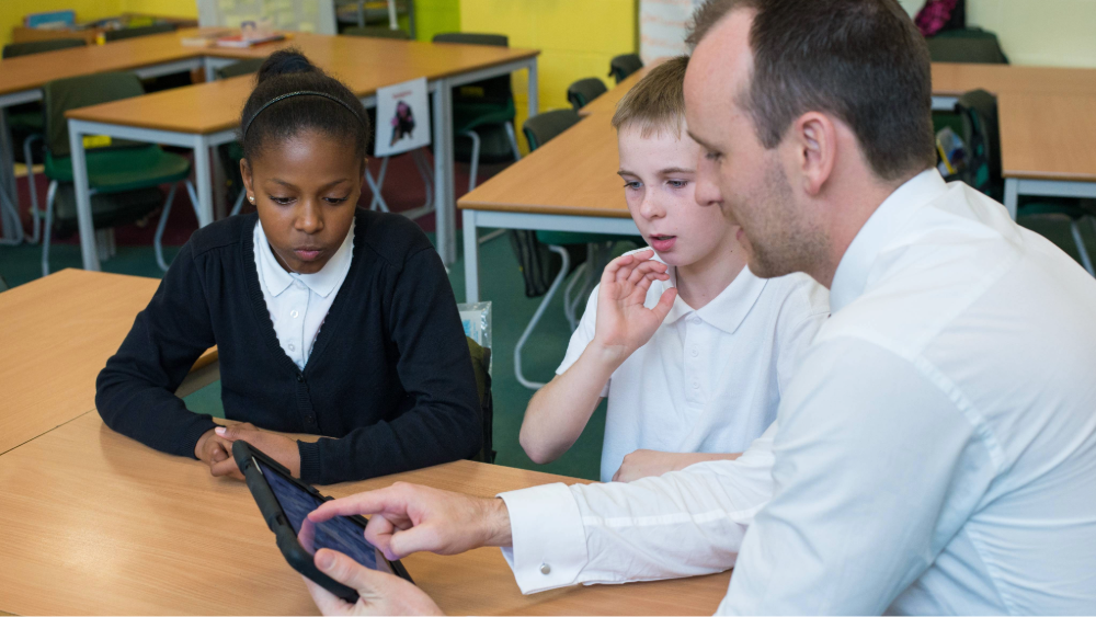 Two secondary students working with a teacher on a tablet in the classroom